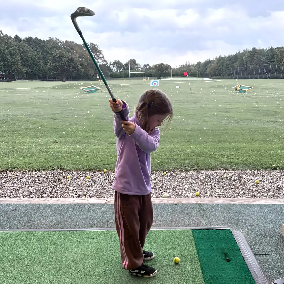 A junior golfer at the top of her swing on the range